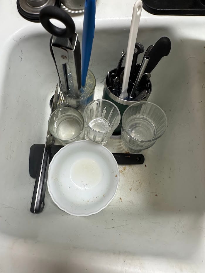 A kitchen sink full of dishes before the clean.