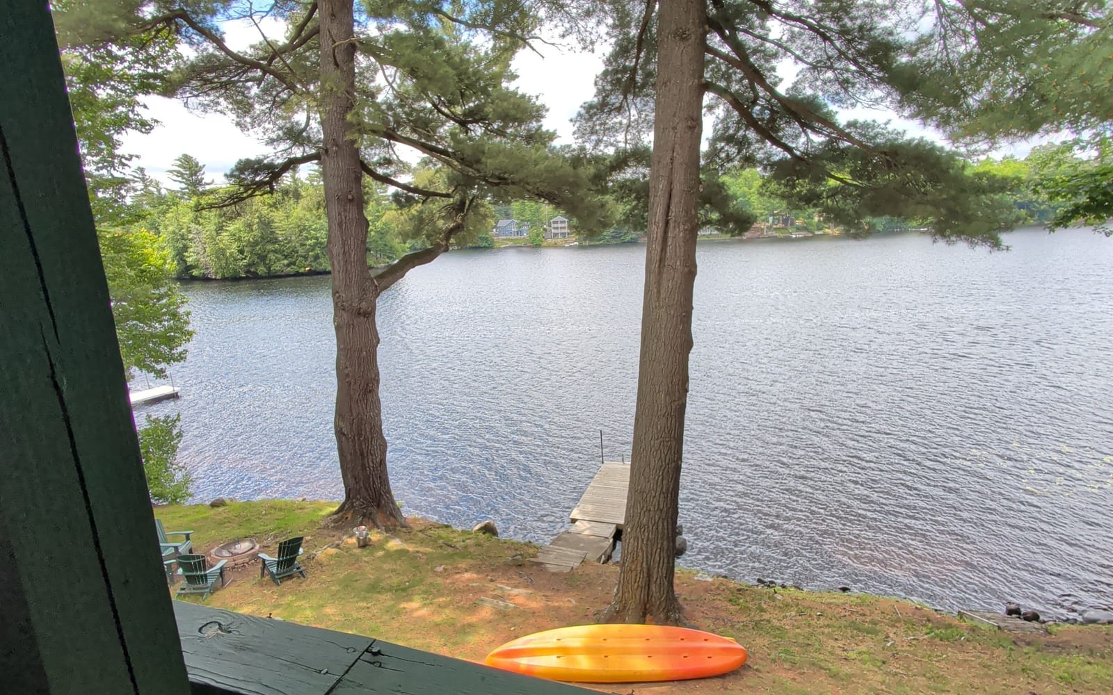The lake from a covered porch: pines, a dock, a kayak on the bank.